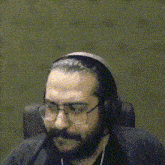 a man with a beard and glasses is wearing headphones and sitting in a chair .