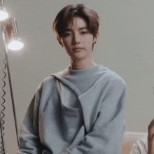 a young man wearing a blue sweater is standing in front of a lamp and looking at the camera .