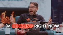 a man is sitting in a chair with a laptop and a microphone and says `` i 'm cooking right now ''