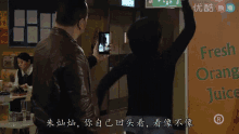 a man taking a picture of a woman in front of a sign that says fresh orange juice