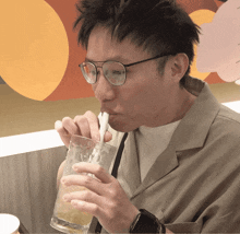 a man wearing glasses drinks through a straw