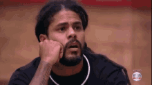 a man with dreadlocks and a beard is sitting on a basketball court with his hand on his chin .