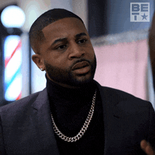 a man wearing a black turtleneck and a silver chain is standing in front of a barber shop