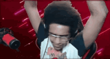 a man wearing headphones and glasses is standing in front of a microphone with his arms in the air .