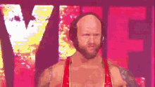 a bald man wearing headphones and a red outfit is standing in front of a large pink sign .