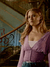 a woman in a purple top stands in front of stairs