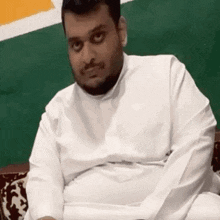 a man with a beard is sitting on a couch wearing a white shirt and making a funny face .