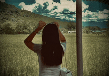 a woman adjusts her glasses in front of a grassy field
