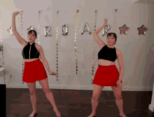 two women in red skirts are dancing in front of balloons that spell out roar