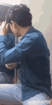 a man in a blue shirt is sitting in front of a mirror and touching his hair