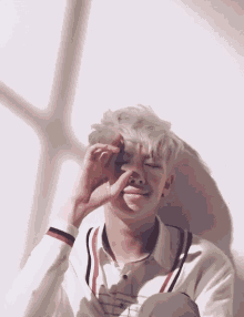 a young man with gray hair is covering his eyes with his hand