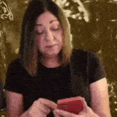 a woman in a black shirt is holding a red cell phone .