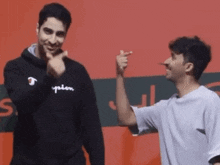 a man wearing a black champion sweatshirt points at another man in a white shirt