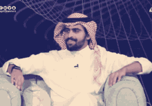 a man wearing a head scarf is sitting in a chair with a microphone on his neck