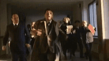 a group of men in suits and ties are dancing in a hallway .