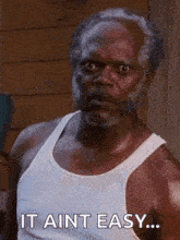 a man with a beard is wearing a white tank top and saying `` it ain 't easy ... '' .