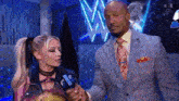 a man in a suit and tie is talking to a woman in a ponytail on a stage .