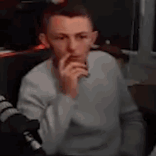 a man in a gray sweater is sitting in a dark room with his hand on his chin .