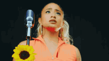 a woman singing into a microphone while holding a yellow flower