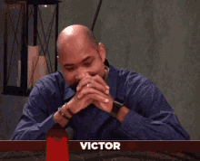 a man with a beard is sitting at a table with a red x in the corner that says victor