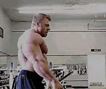 a man is flexing his muscles in a gym while standing in front of a mirror .