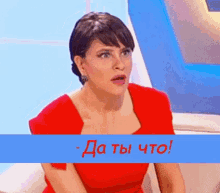 a woman in a red dress is sitting in front of a blue banner that says да ты что