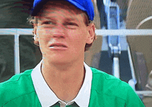 a man wearing a green shirt and a blue hat makes a funny face