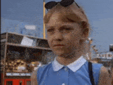 a girl wearing sunglasses and a blue shirt is standing in front of a carnival booth