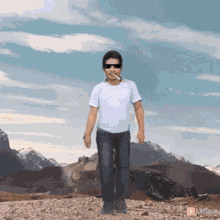 a man wearing sunglasses and a cigarette in his mouth is standing in front of mountains