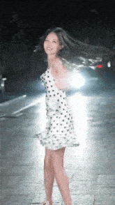 a woman in a white polka dot dress is dancing on a sidewalk at night .