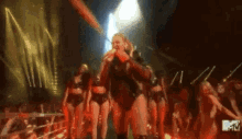 a woman is singing into a microphone on a stage in front of a group of dancers .