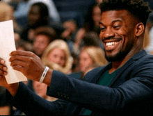 a man in a suit is smiling while holding a piece of paper in front of a crowd