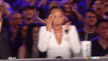 a woman in a white dress is covering her face in front of a crowd of people on a show called agt