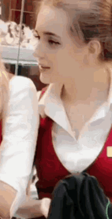 a woman wearing a red vest and a white shirt is sitting at a table .