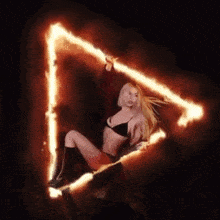 a woman in a black bra is holding a triangle of fire in her hand .