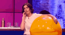 a woman is sitting on a stage with a large orange ball .