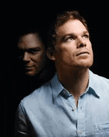 a man in a blue shirt is standing in front of another man in a dark room .