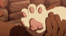 a person is petting a cat 's paw with a brick wall in the background