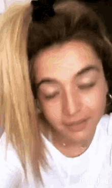 a close up of a woman 's face with her eyes closed . she is wearing a white shirt and earrings .