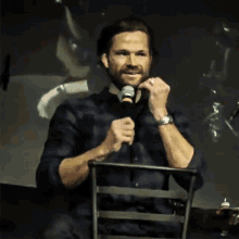 a man sitting in a chair holding a microphone and covering his mouth