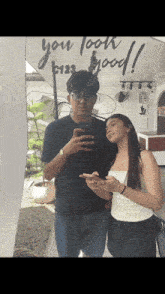 a man and a woman are taking a picture in front of a sign that says you look good