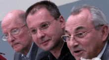 three men wearing glasses are standing next to each other and looking at the camera .