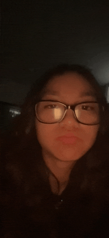 a woman wearing glasses and headphones is taking a selfie in the dark .