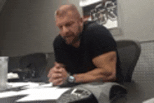 a man is sitting at a desk with his hands folded and a watch on his wrist .