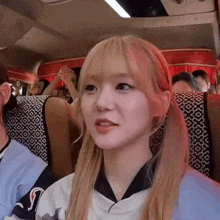 a young girl with blonde hair is sitting on a bus with other people .