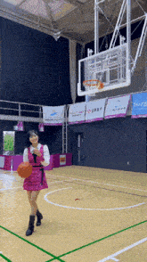 a girl in a pink dress is holding a basketball in a basketball court