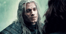 a man with long white hair is talking to a woman in a leather jacket .