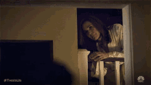 a woman leaning on a railing in a dark room with a nbc logo on the bottom