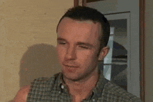 a man in a plaid shirt is standing in front of a door and looking at the camera .