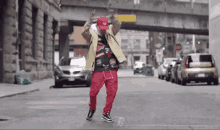 a man wearing a red hat and red pants is dancing on the street .